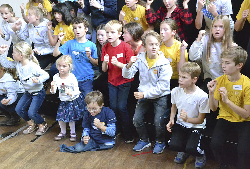 Kinder singen fröhlich ein Lied und machen Bewegungen dazu.